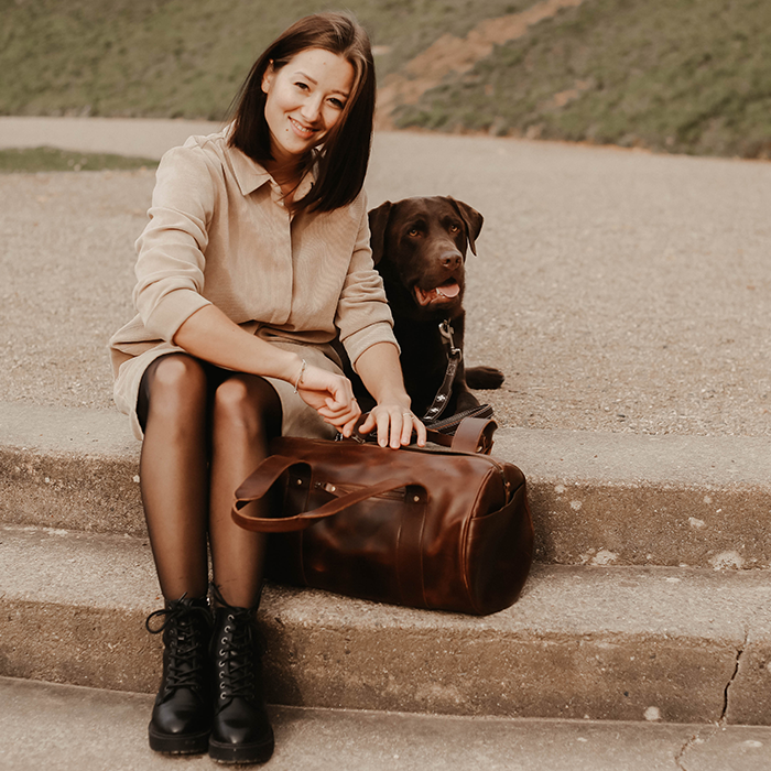 Frau mit Hund zeigt ihre hochwertige Ledertasche im Park