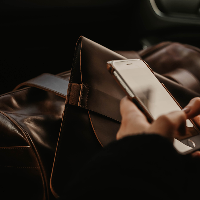 Jemand ist am Handy und zu sehen sind hochwertige Ledertaschen im Auto